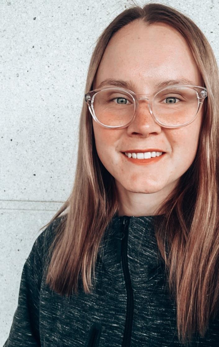 Hilma seisoo vaaleaa seinää vasten ja hymyilee.