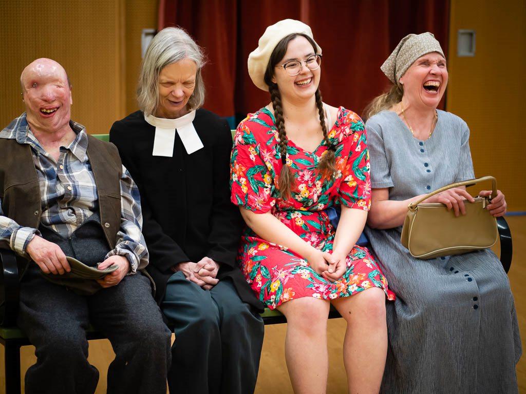 Neljä naista istuu penkillä ja nauraa makeasti