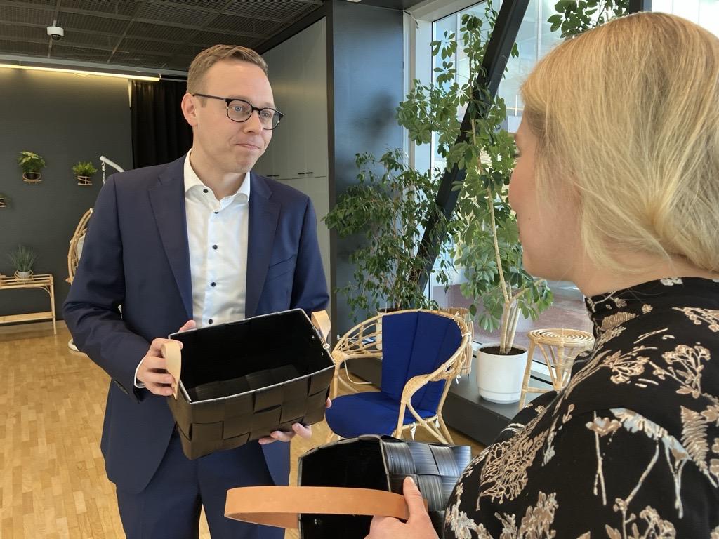 Työministeri Matias Marttinen tarkastelee mustaa Annansilmät-Aitan käsintehtyä koria ja keskustelee Iiris Pron yksikönvastaava Tuuli Kulosen kanssa.