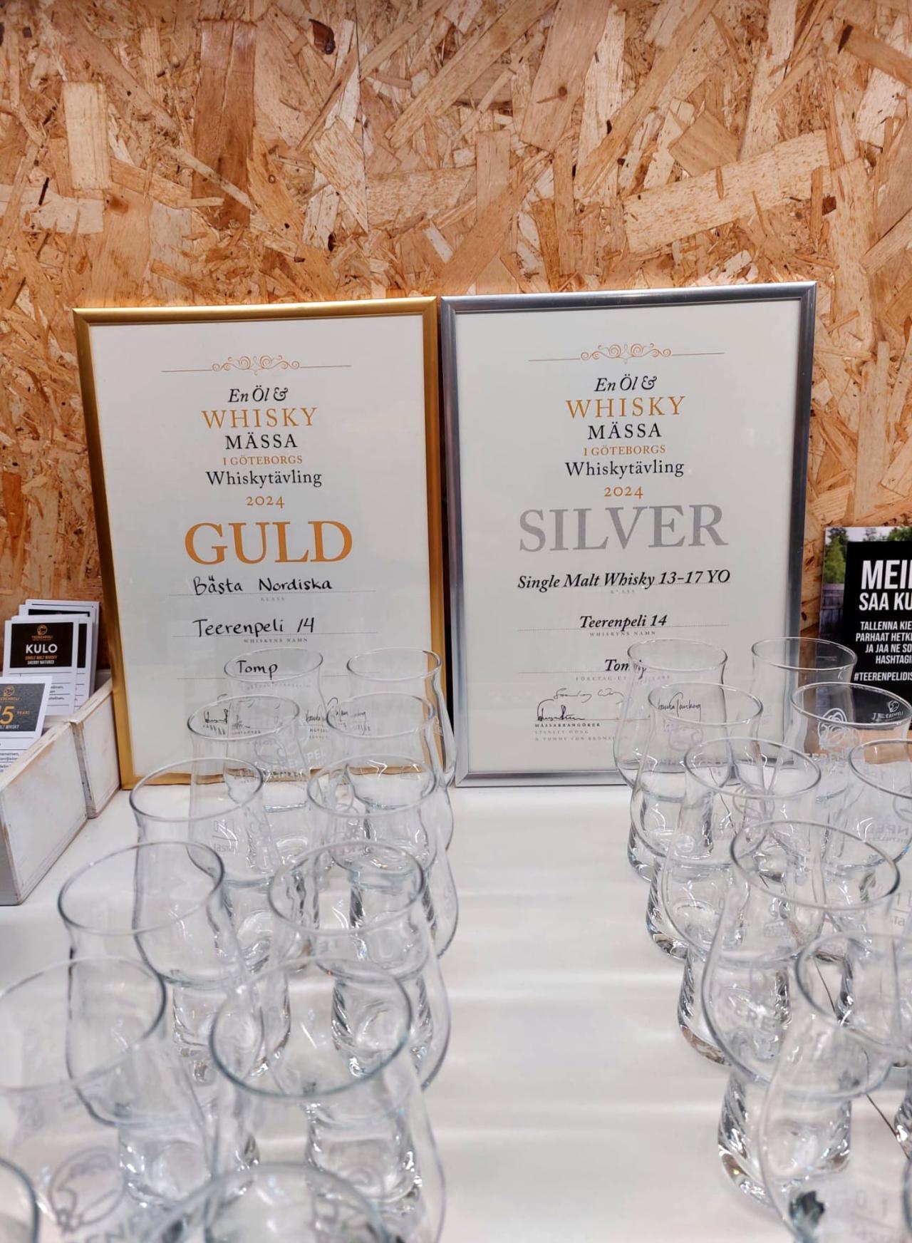 Kuva etualalla läpinäkyviä viskilaseja. Taustalla vasemmalla kultareunainen viski diplomi ja oikealla hopeareunainen viski diplomi.