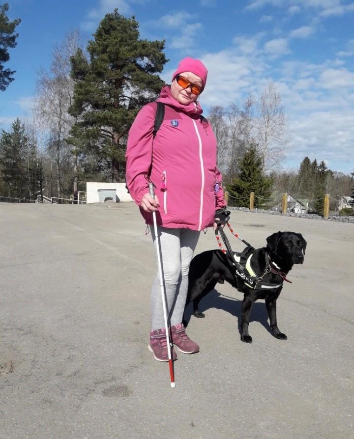 Susanna seisoo musta opaskoira vierellään ja valkoinen keppi kädessään. Hän katsoo kameraan.