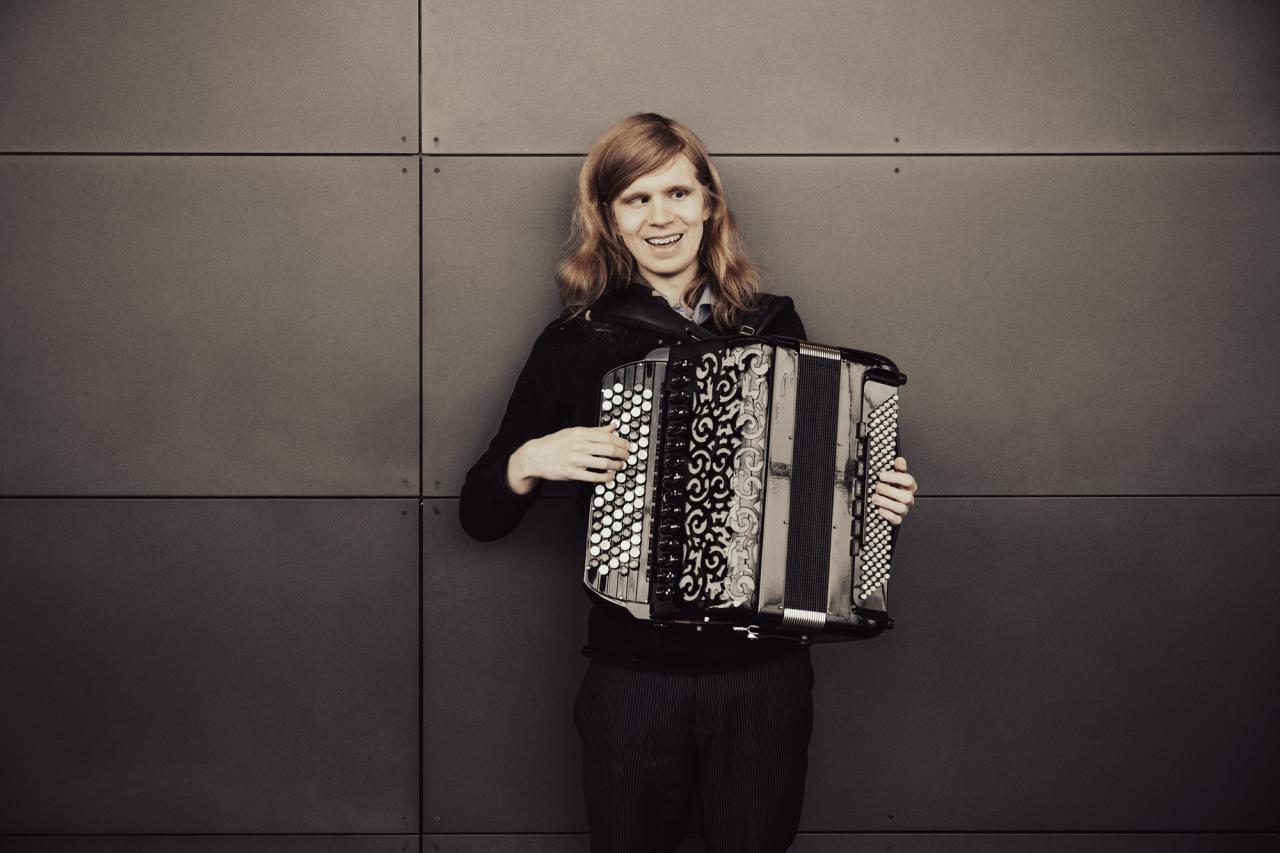 Joose Ojala Musiikkitalon seinää vasten haitari sylissään.