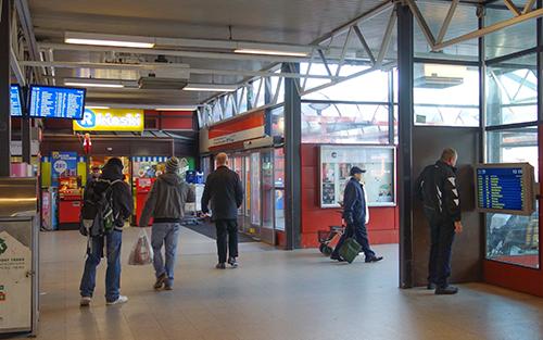 Kuva Itäkeskuksen metroasemalta. Mies katsoo läheltä pään korkeudella olevaa aikataulunäyttöä kuvan oikeassa reunassa. Vasemmassa reunassa vastaava näyttö on korkealla.