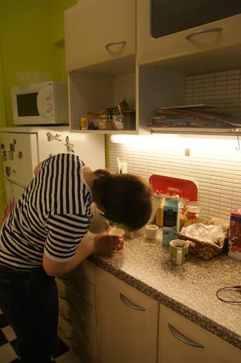 Nuori nainen kaataa vedenkeittimestä vettä kuppiin keittiössä.