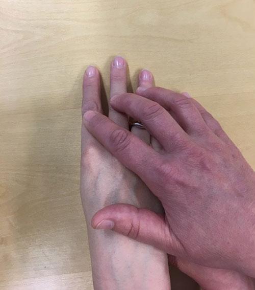 Ohjaajan käsi on oppilaan kolmen sormen ja kämmenselän päällä.