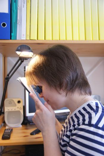 Nuori nainen lukee lehteä luupin avulla.