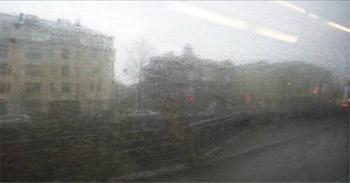 Likainen bussin ikkuna, jonka läpi näkyy sumeasti kaupunkimaisemaa.