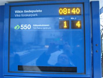 Pysäkillä oleva näyttö, jossa näkee linja-auton numeron ja montako minuuttia on kunnes seuraavat kaksi bussia tulevat. Näytössä on myös kello.