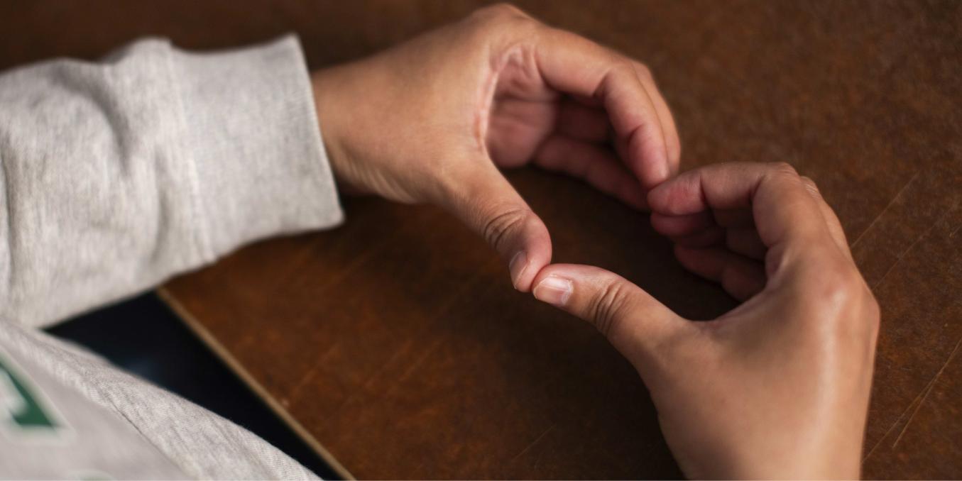 Lähikuva pöydän päälle asetetuista käsistä, jotka muodostavat sydämen