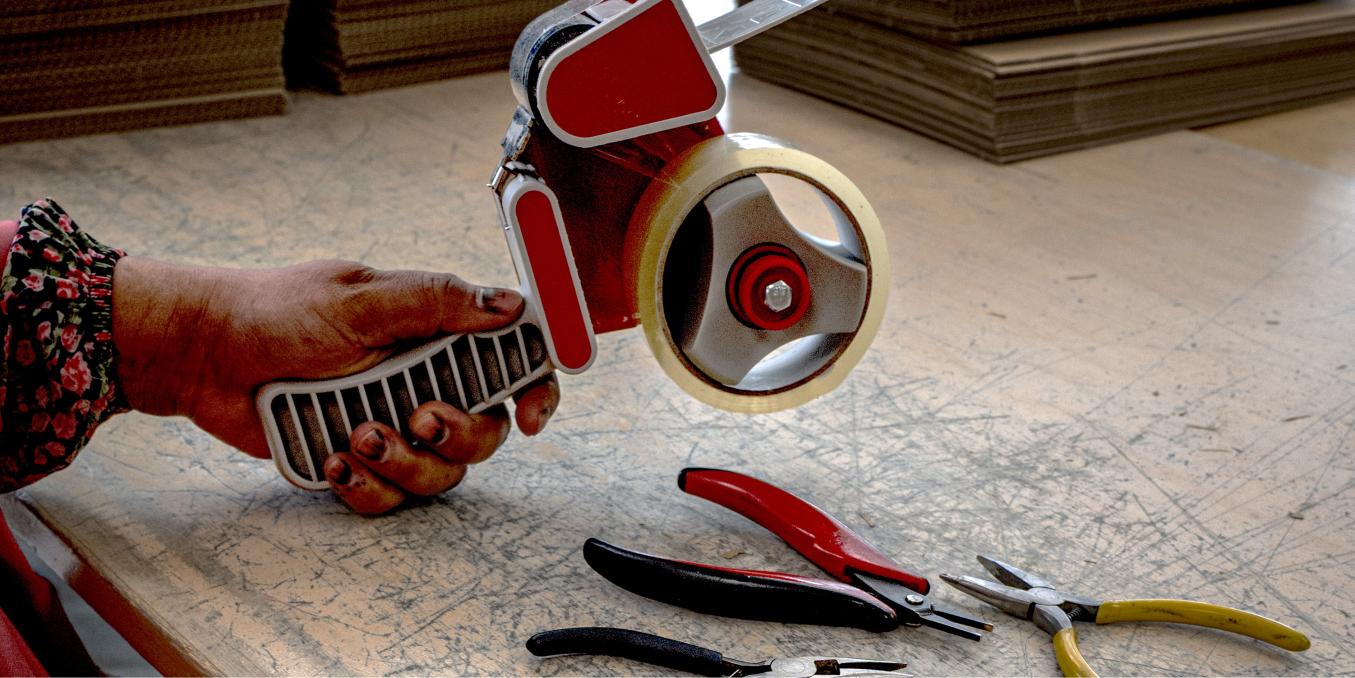 Lähikuva kädesta, joka pitelee teippikonetta kauniisti kuluneen puupöydän päällä.