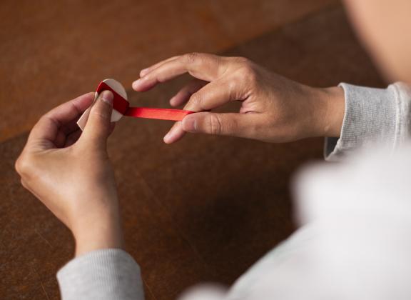 Lähikuva käsistä sitomassa punaista satiininauhaa.